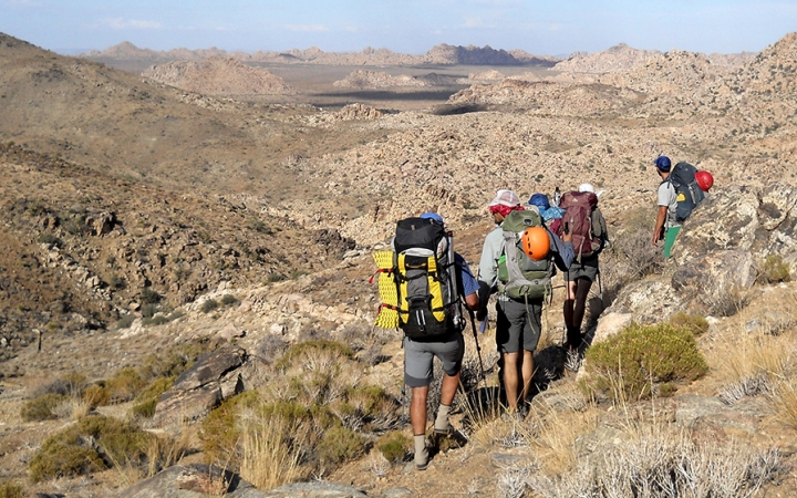a group of backpackers make their way through a desert landscape on an outward bound course